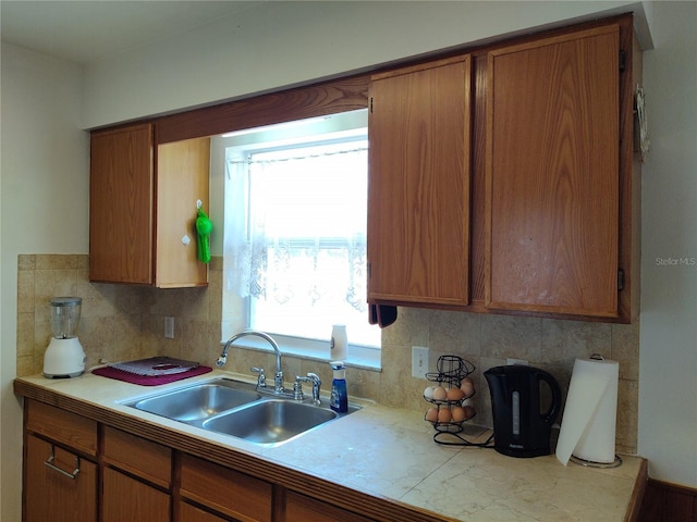 kitchen featuring light countertops, backsplash, brown cabinetry, and a sink