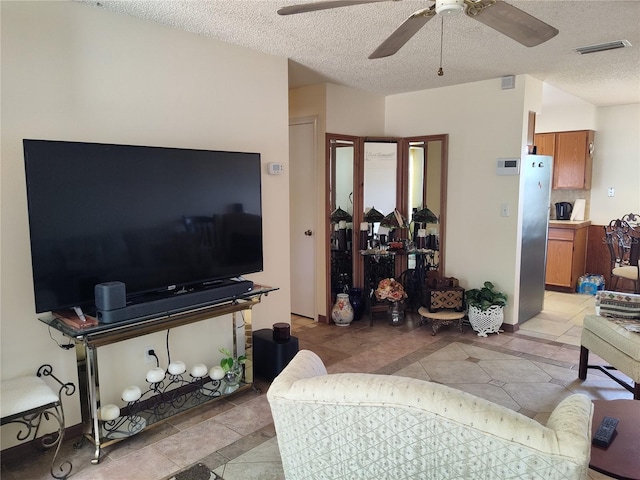 living area with a textured ceiling, ceiling fan, visible vents, and light tile patterned floors