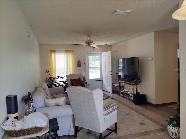 living room with visible vents, light tile patterned flooring, baseboards, a textured ceiling, and a ceiling fan