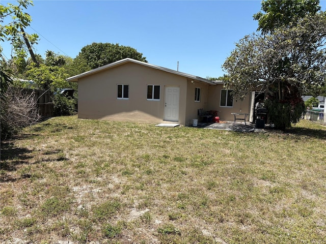 rear view of house with fence, a patio, stucco siding, and a lawn