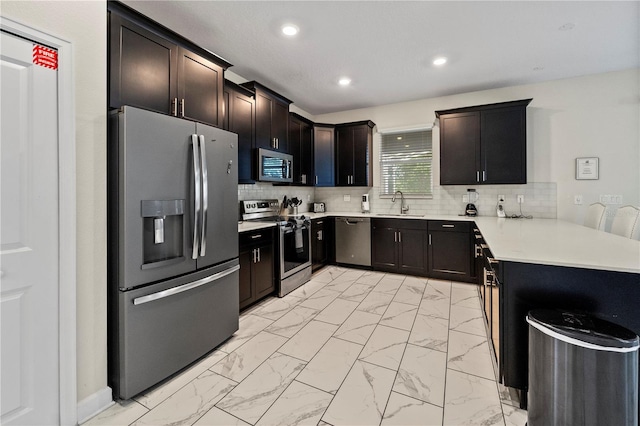 kitchen with stainless steel appliances, light marble finish floors, a peninsula, a sink, and light countertops