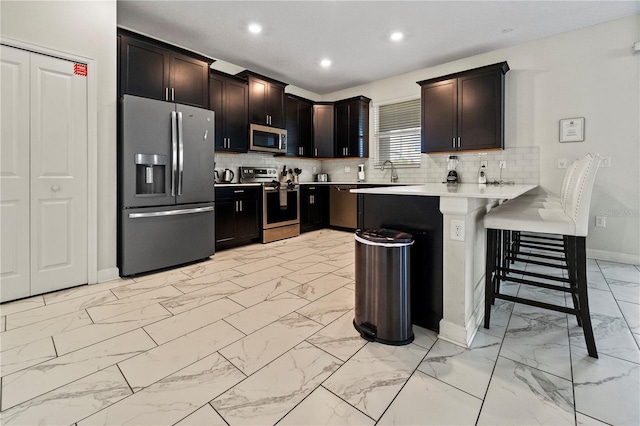 kitchen featuring appliances with stainless steel finishes, light marble finish floors, baseboards, a peninsula, and light countertops