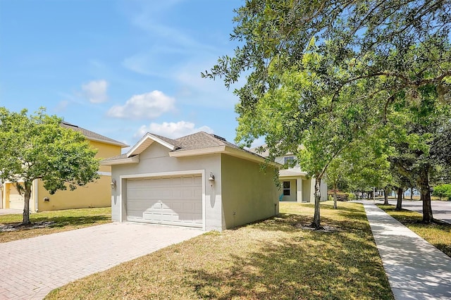 ranch-style house with decorative driveway, an attached garage, a front lawn, and stucco siding