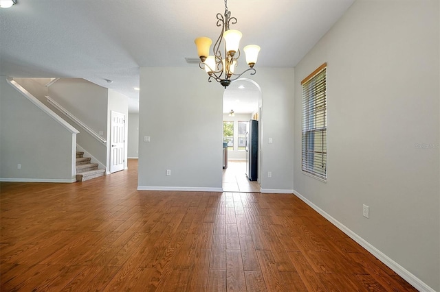 empty room featuring an inviting chandelier, visible vents, stairs, wood finished floors, and baseboards