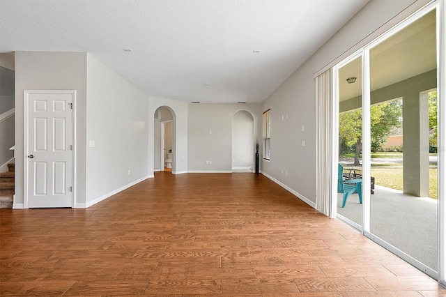 empty room with arched walkways, baseboards, stairs, and wood finished floors