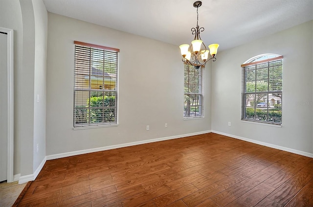 empty room with wood-type flooring, baseboards, a notable chandelier, and a wealth of natural light