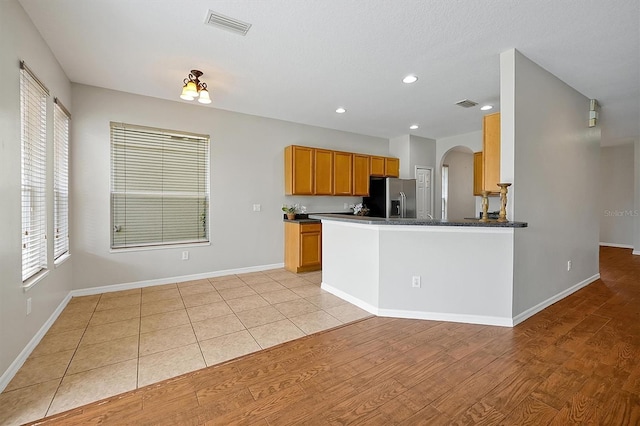 kitchen with stainless steel fridge, arched walkways, light wood finished floors, and visible vents
