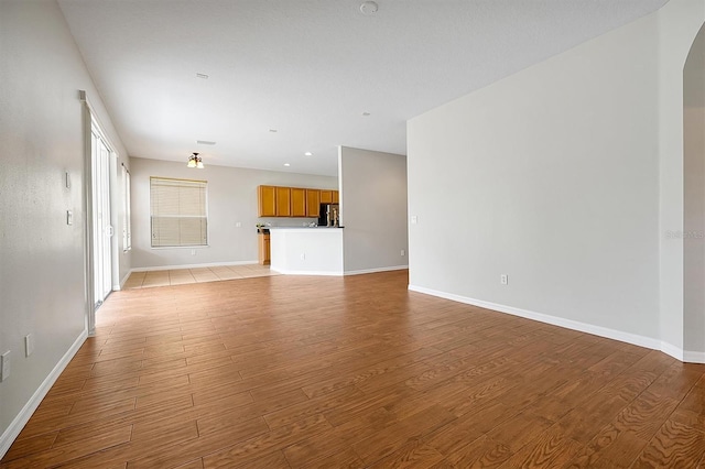 unfurnished living room featuring arched walkways, baseboards, recessed lighting, and light wood finished floors