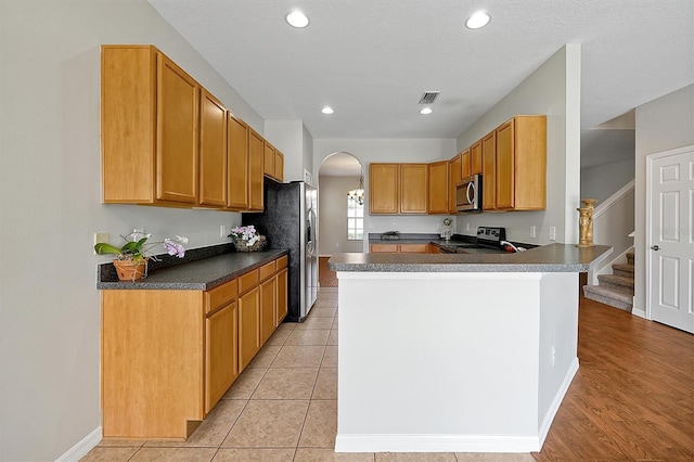 kitchen featuring visible vents, a peninsula, dark countertops, arched walkways, and appliances with stainless steel finishes