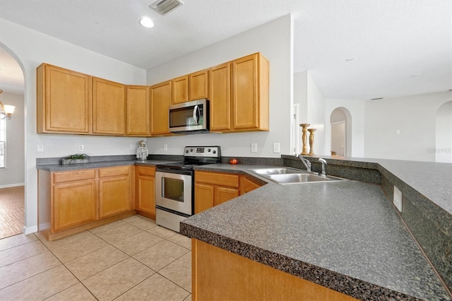 kitchen featuring dark countertops, a sink, arched walkways, stainless steel appliances, and visible vents