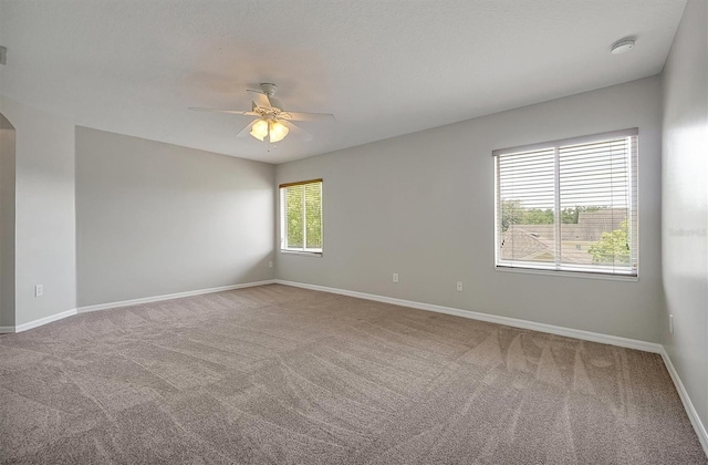 empty room with baseboards, arched walkways, carpet, and ceiling fan