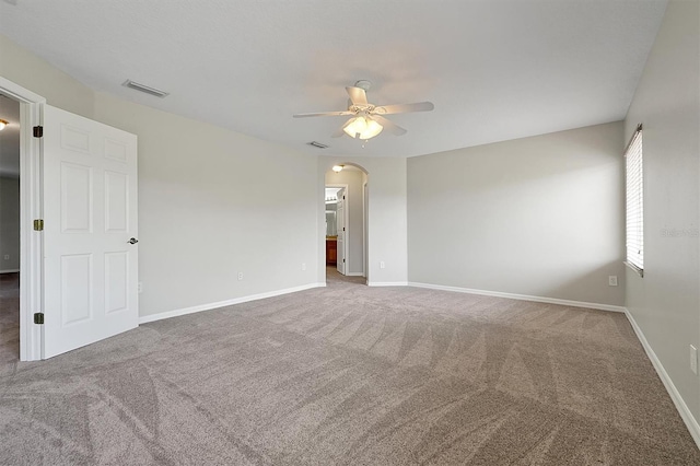 carpeted empty room with visible vents, a ceiling fan, baseboards, and arched walkways