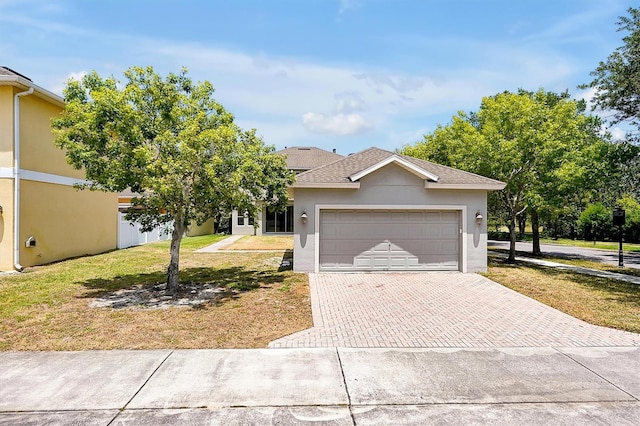 view of front of house with an attached garage, decorative driveway, a front lawn, and stucco siding