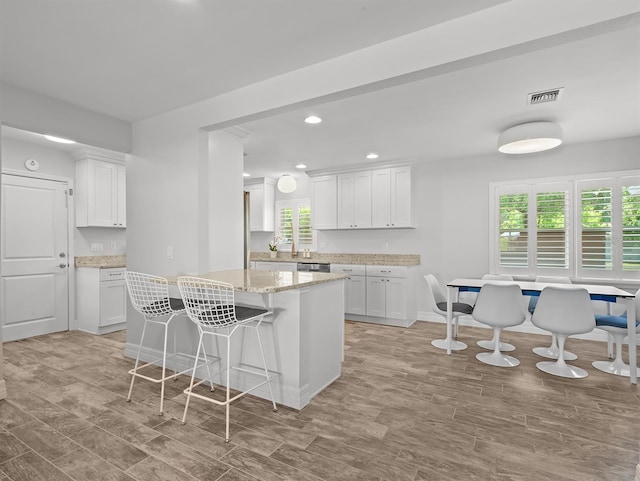 kitchen featuring white cabinetry, light wood-type flooring, a breakfast bar, visible vents, and dishwasher