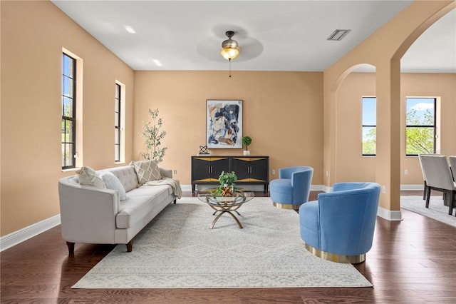 living area featuring a ceiling fan, visible vents, baseboards, arched walkways, and dark wood finished floors