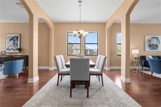 dining room featuring wood finished floors, baseboards, a chandelier, and arched walkways
