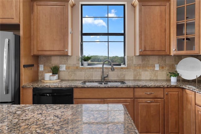 kitchen featuring glass insert cabinets, a sink, freestanding refrigerator, dishwasher, and brown cabinetry