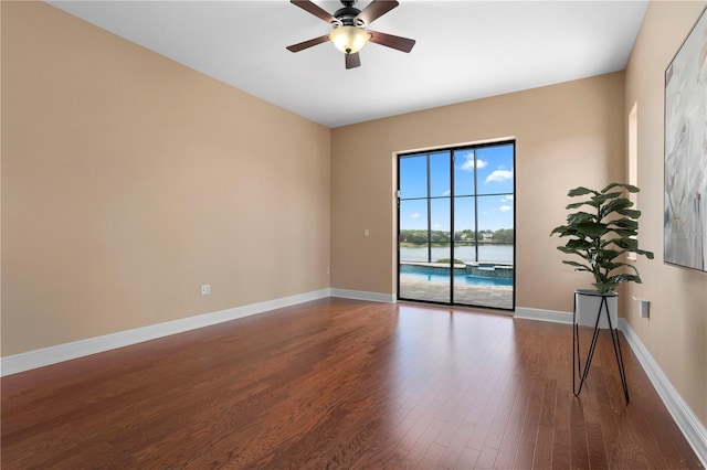 empty room with baseboards, wood finished floors, ceiling fan, and a water view
