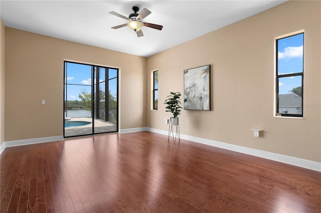 unfurnished room featuring dark wood-type flooring, ceiling fan, a water view, and baseboards