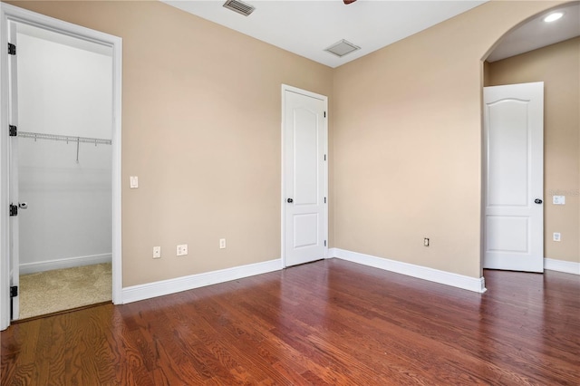 unfurnished bedroom with arched walkways, wood finished floors, a walk in closet, baseboards, and visible vents