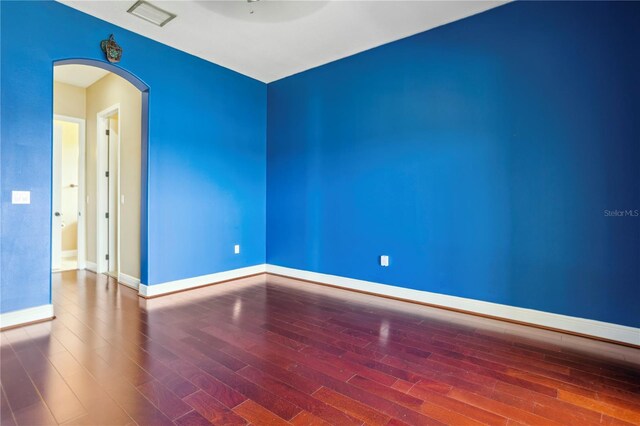 unfurnished room featuring wood finished floors, baseboards, visible vents, and arched walkways