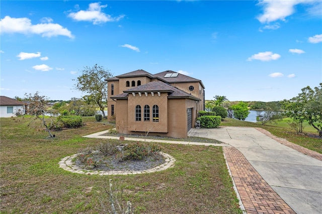 view of front of property with a front lawn, a water view, driveway, roof mounted solar panels, and stucco siding