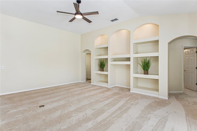spare room featuring arched walkways, carpet floors, ceiling fan, and built in shelves