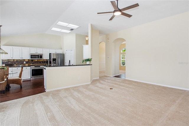 kitchen featuring open floor plan, white cabinetry, stainless steel appliances, dark countertops, and arched walkways