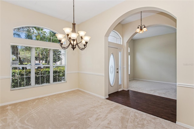 carpeted foyer featuring an inviting chandelier, arched walkways, baseboards, and wood finished floors