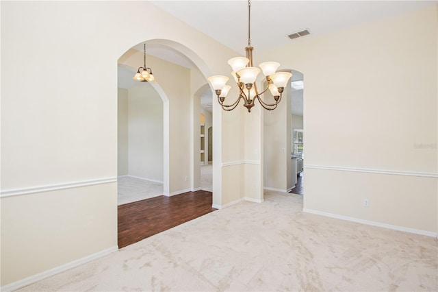 unfurnished room with carpet flooring, visible vents, baseboards, arched walkways, and a notable chandelier