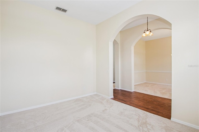 spare room with wood finished floors, arched walkways, baseboards, and visible vents