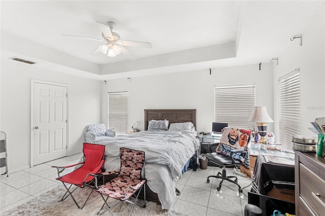 bedroom with a tray ceiling, light tile patterned floors, a ceiling fan, and visible vents