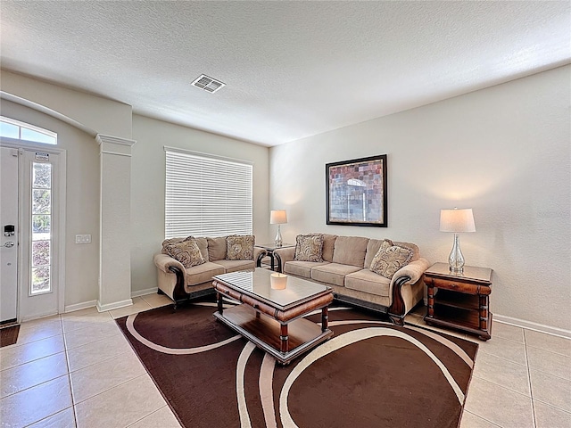 living area featuring a textured ceiling, light tile patterned floors, baseboards, and visible vents