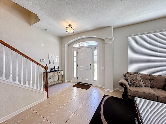 foyer featuring light tile patterned floors, baseboards, stairway, and a textured ceiling