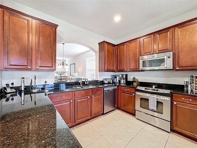 kitchen featuring light tile patterned floors, arched walkways, dark stone countertops, a sink, and stainless steel appliances