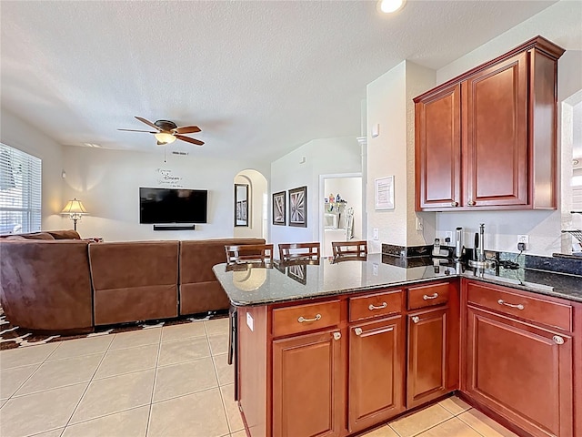 kitchen featuring open floor plan, dark stone countertops, ceiling fan, and light tile patterned flooring