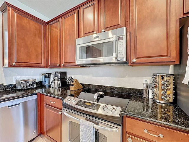 kitchen featuring stainless steel appliances, brown cabinetry, and dark stone countertops