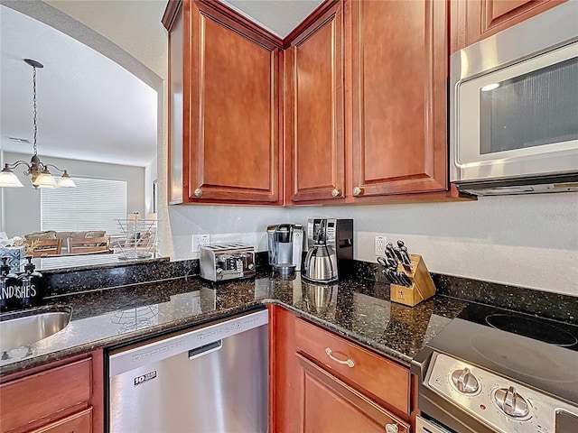kitchen with a notable chandelier, decorative light fixtures, a sink, dark stone counters, and stainless steel appliances