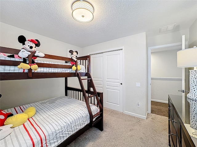 carpeted bedroom with a closet, visible vents, baseboards, and a textured ceiling