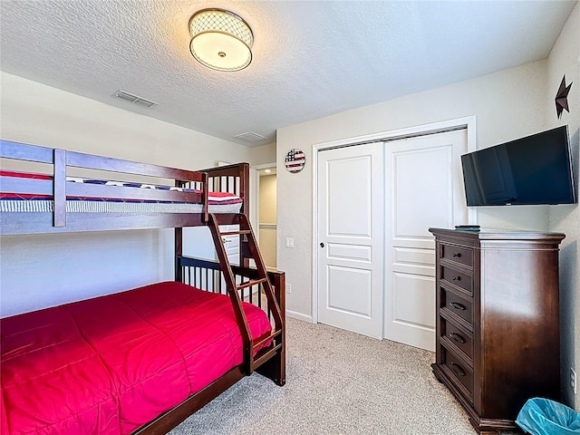 bedroom featuring visible vents, a closet, light carpet, and a textured ceiling