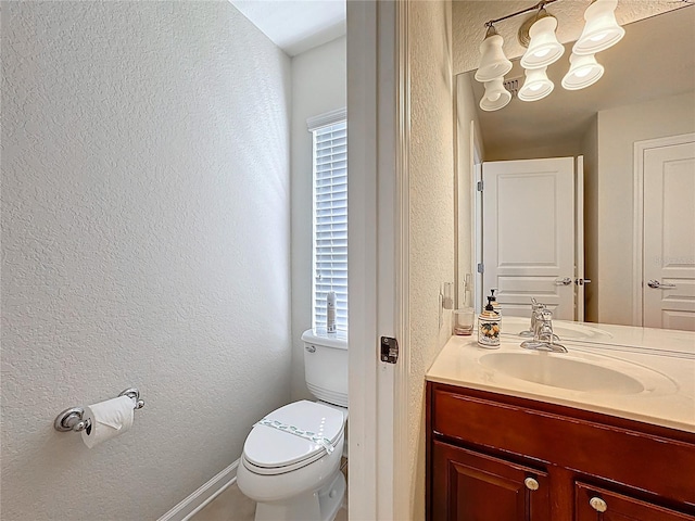 half bathroom with toilet, vanity, a textured wall, and baseboards