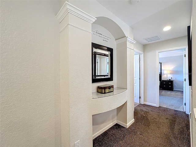 corridor with visible vents, baseboards, dark colored carpet, and a textured wall