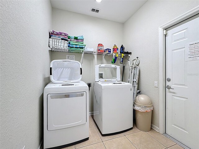 laundry room with a textured wall, light tile patterned floors, visible vents, laundry area, and washing machine and clothes dryer