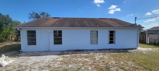 rear view of house featuring fence and a shingled roof