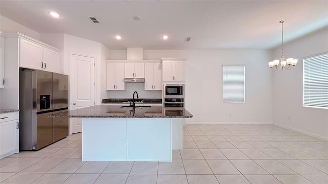 kitchen featuring dark stone counters, under cabinet range hood, a healthy amount of sunlight, a sink, and stainless steel appliances