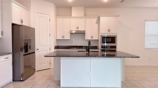 kitchen featuring dark stone counters, white cabinets, under cabinet range hood, a sink, and stainless steel appliances