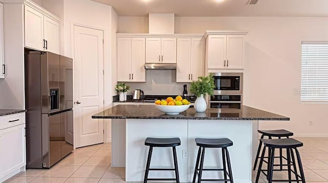 kitchen with refrigerator with ice dispenser, under cabinet range hood, built in microwave, a breakfast bar area, and stainless steel oven