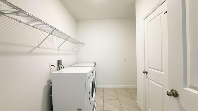 clothes washing area with baseboards, washer and dryer, light tile patterned flooring, and laundry area