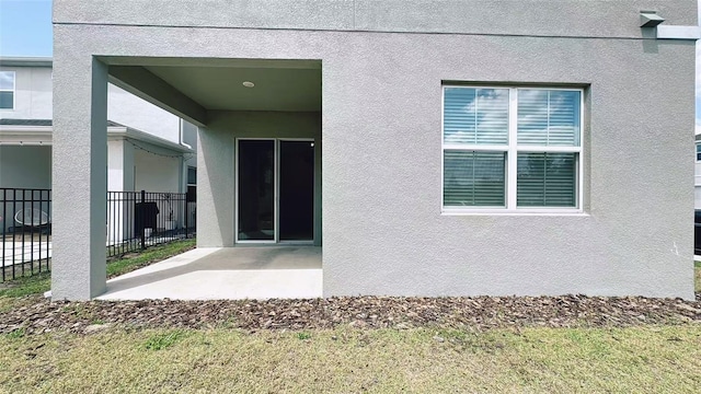 view of exterior entry with fence, a patio, and stucco siding
