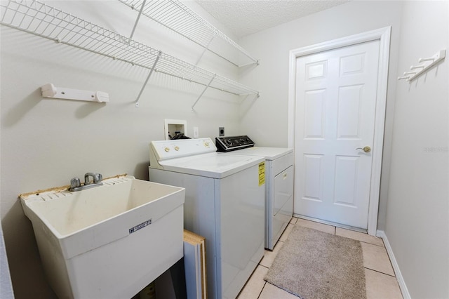 laundry room with light tile patterned floors, a sink, laundry area, washer and clothes dryer, and baseboards